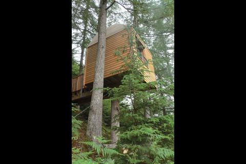 The studio, built of larch timber, is positioned on top of a tree trunk and anchored to the slope.